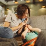 Jak reagować, gdy senior nie odbiera telefonu: procedura, która może uratować życie Matka rozmawia przez telefon, tuląc dziecko na kanapie w salonie