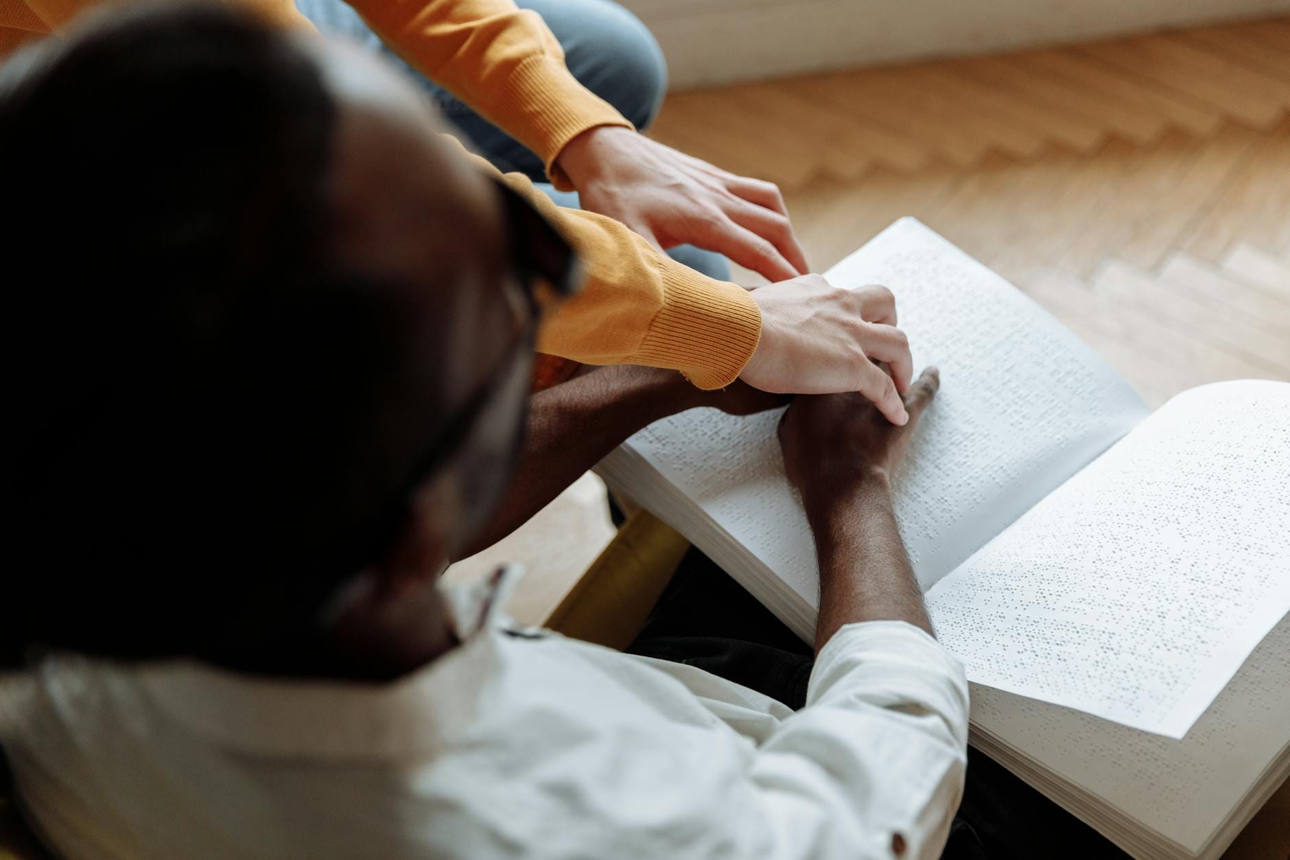 Mentor pomaga niewidomemu mężczyźnie czytać książkę w alfabecie Braille’a