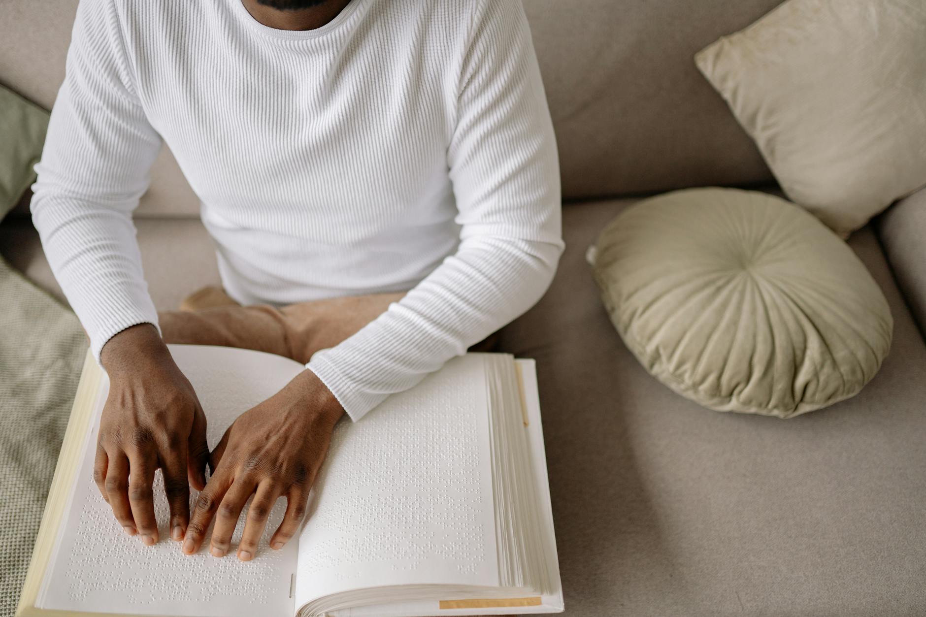 Osoba w białym swetrze czyta książkę w alfabecie Braille’a na kanapie